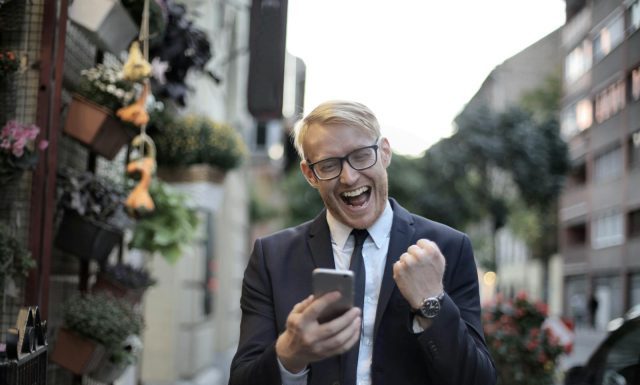 Avoid These Golden Slipper Betting Pitfalls for Smarter Wagers Excited young man in formal wear and eyeglasses clenching fist and rejoicing victory while using mobile phone in modern city street