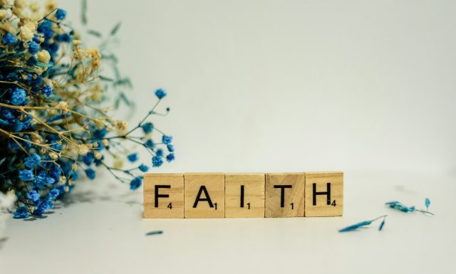 The Role of Faith in Coping with Life’s Difficulties a wooden block that says faith next to blue flowers